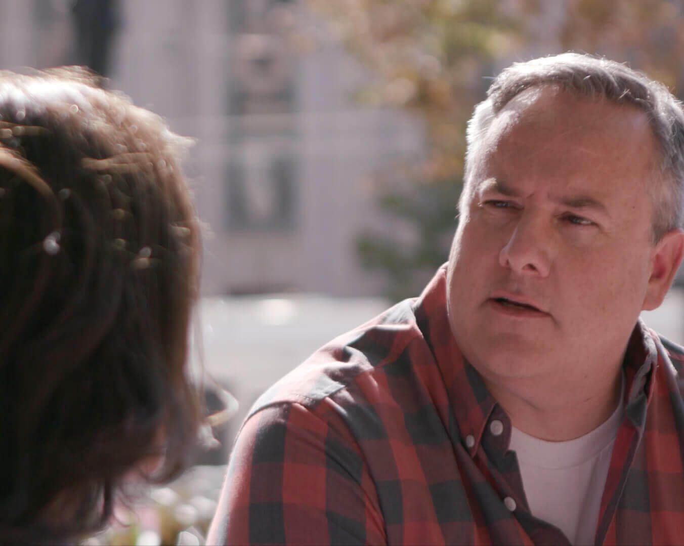 Man In a Red And Black Plaid Shirt Talking To a Woman Outside