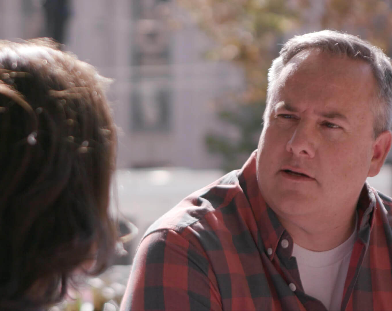 Man In a Red And Black Plaid Shirt Talking To a Woman Outside